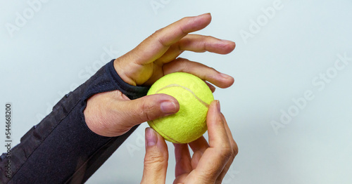 Broken hand in black orthosis holding a yellow tennis ball for training and recovery on light gray background photo