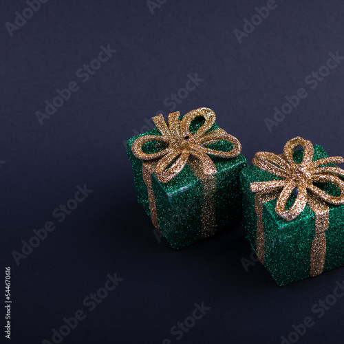 Christmas decor green gift box with shiny gold bow on dark square background photo