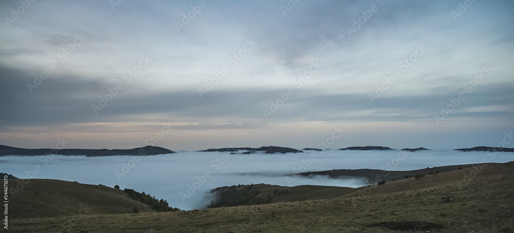 Panorama of mountain hills and rows with low clouds and fog in the valley between the mountains, in the early morning in the mountains Panorama of mountain hills and rows with low clouds and fog in the valley between the mountains, in the early morning in the mountains