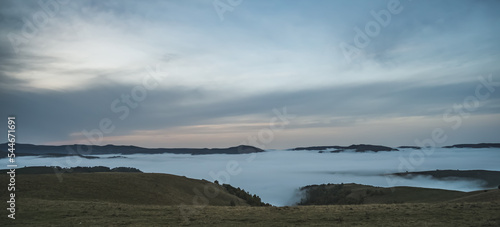 Panorama of mountain hills and rows with low clouds and fog in the valley between the mountains, in the early morning in the mountains © Denis