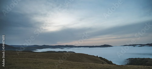 Fototapeta Naklejka Na Ścianę i Meble -  Panorama of mountain hills and rows with low clouds and fog in the valley between the mountains, in the early morning in the mountains