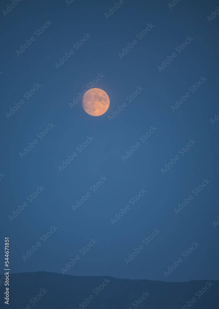 Full moon in the mountains in the early morning with a mountain cliff and dense clouds in the valley, orange moon in the autumn morning in the mountains Full moon in the mountains in the early morning with a mountain cliff and dense clouds in the valley, orange moon in the autumn morning in the mountains
