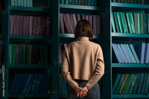Apathy and frustration. Cognitive overload from an overabundance of news and information noise, concept. Back view of a woman standing with her face buried in bookshelves.