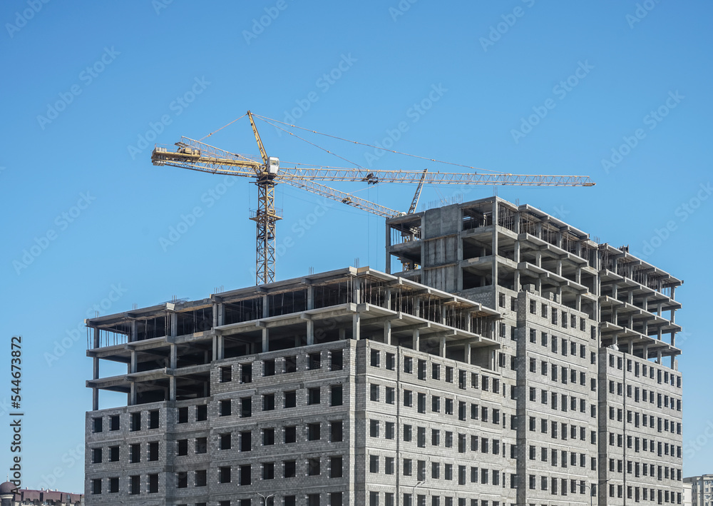 Tower cranes and unfinished buildings on background of blue sky with white clouds. Housing construction, apartment blocks in city.