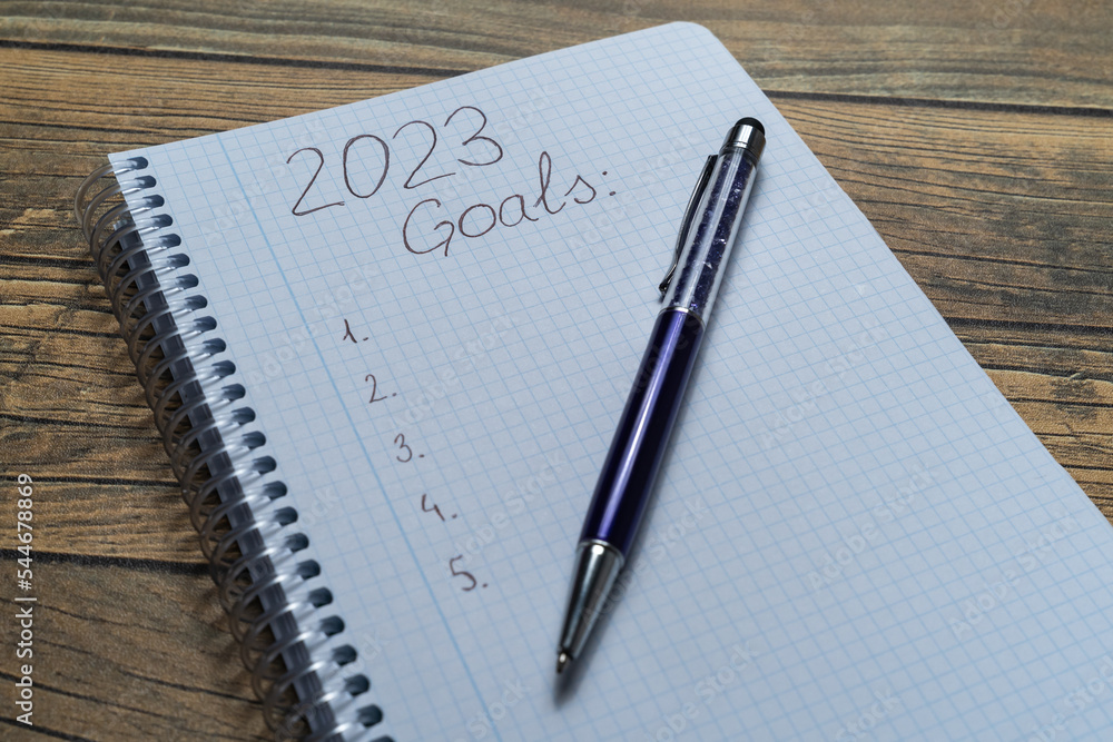 Notebook sheet written 2023 to put the resolutions and objectives of the year, with a pen and wooden background. Notebook sheet written 2023 to put the resolutions and objectives of the year, with a pen and wooden background.