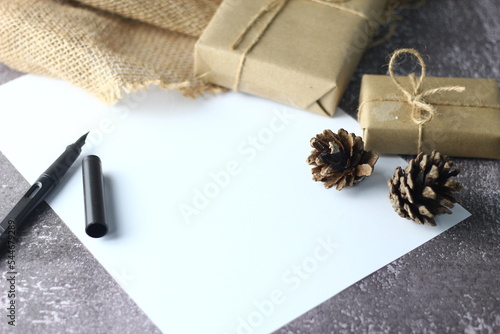 Holidays Gifts. Christmas and New Year..Gift box wrapped in brown paper, pine cones and white paper and pens placed on the table, copy space.