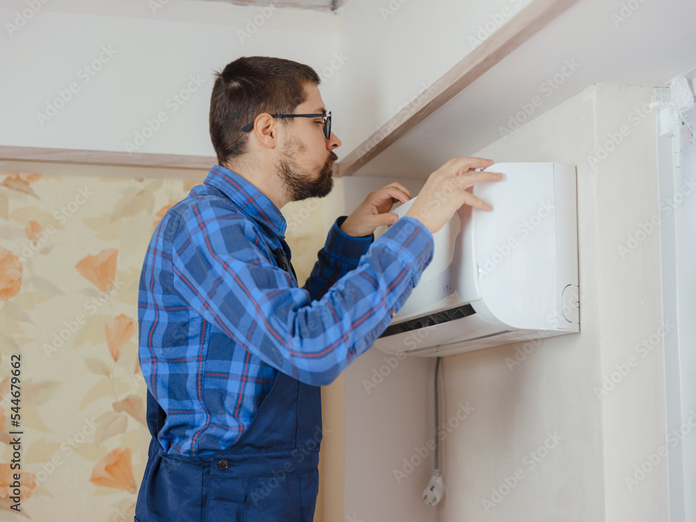 young man in blue work suit doing Repair apartment. Home renovation concept. Guy Adjusting Air Conditioning System