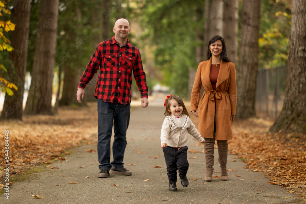 A cute little girl is playfully running away from her parents in a beautiful autumn colored park
