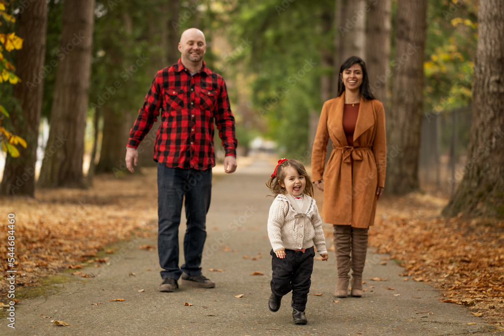 A cute little girl is playfully running away from her parents in a beautiful autumn colored park