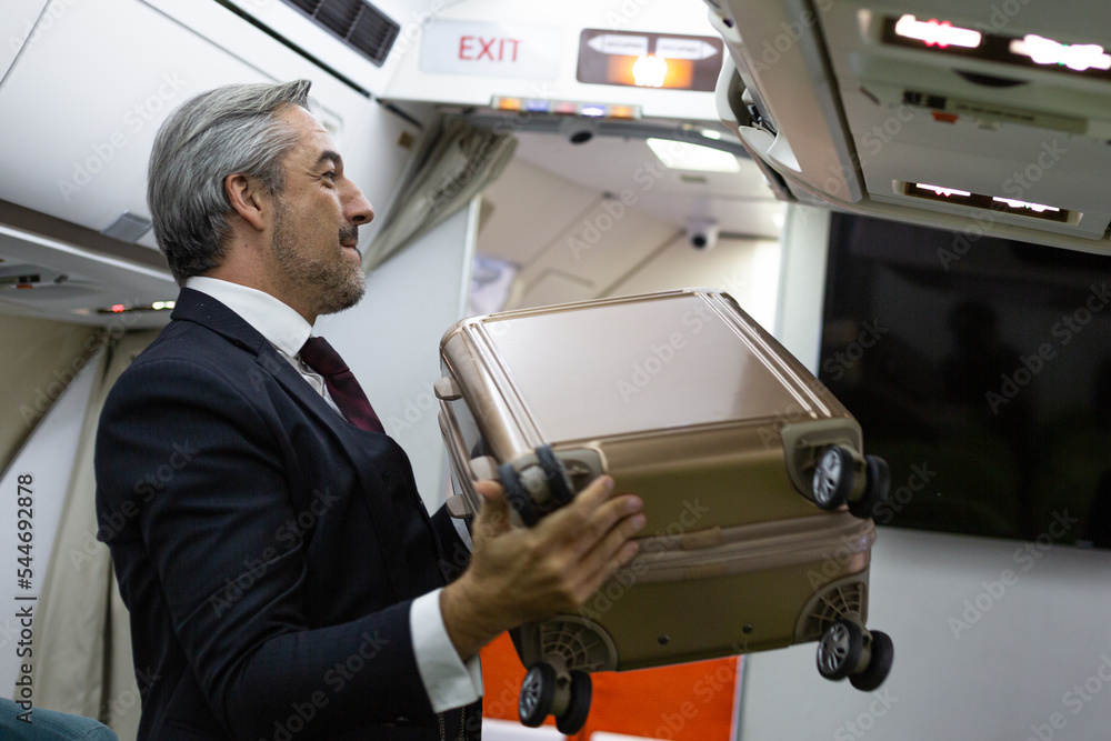 Caucasian business man put cabin luggage into the airplane storage before flight departure Caucasian business man put cabin luggage into the airplane storage before flight departure