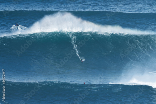 Surfer is riding a giant big wave in Nazare, Portugal. Biggest waves in the world. Touristic destination for surfing and lovers of radical sports. Jet skis in the water. Amazing destinations.