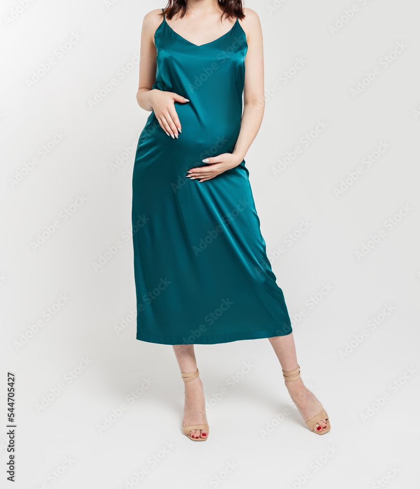 Fototapeta premium Pregnant girl in a fashionable elegant dress with heels in the studio holding her belly