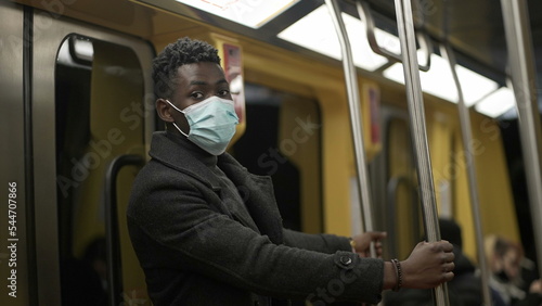 African man adjusting face mask while commuting on train holding bar handrail5