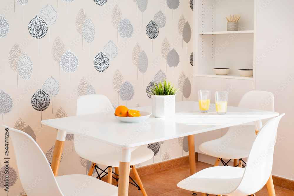 White kitchen table with two glasses of orange juice, a split fresh orange, green natural plant and leaf wallpaper background, in grey, blue and white White kitchen table with two glasses of orange juice, a split fresh orange, green natural plant and leaf wallpaper background, in grey, blue and white