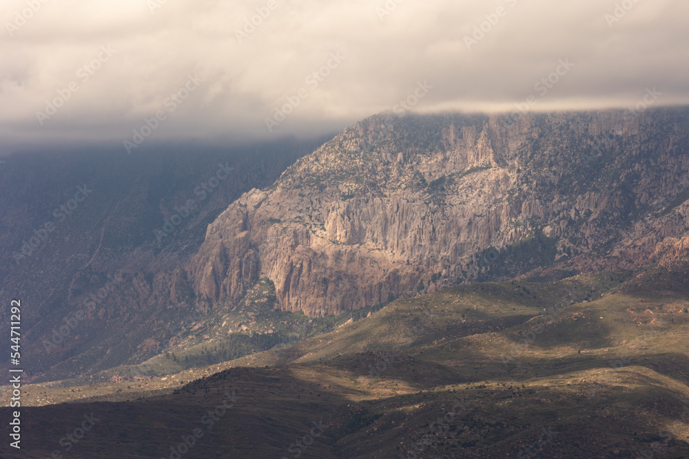 Low clouds cover the top of Pine Valley mountain in Southern Utah while beams of sunlight break through and make the rocky cliffs and tree covered slopes glow.