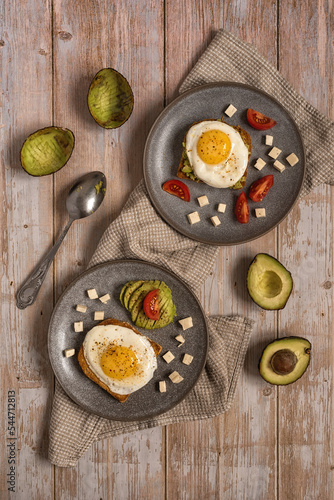 Avocado toast. Healthy breakfast for two: toast bread with fried eggs, avocado, feta cheese and tomato in ceramic plates on a wooden table. Healthy food. Healthy lifestyle. Top view. Flat lay.  photo