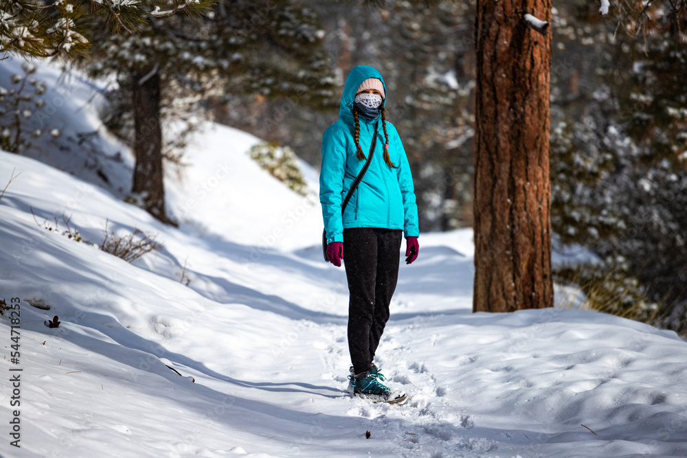 girl in blue jacket hiking among snow-covered trees in bryce canyon national park in winter; magical winter landscape in usa, utah