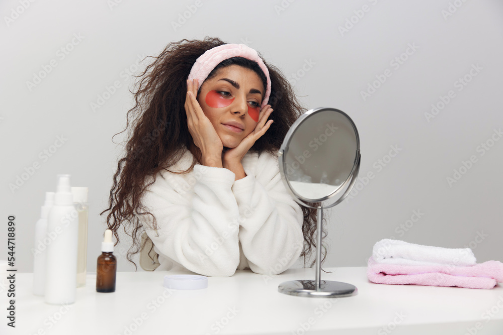 Awesome tanned pretty curly Latin lady with pink patch for eye admiring herself doing beauty procedure in white home interior. Copy space. MIRROR, MIRROR, ON THE WALL, WHO IS THE FAIREST OF THEM ALL Awesome tanned pretty curly Latin lady with pink patch for eye admiring herself doing beauty procedure in white home interior. Copy space. MIRROR, MIRROR, ON THE WALL, WHO IS THE FAIREST OF THEM ALL