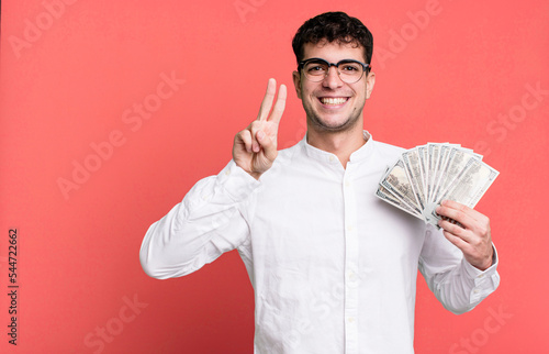 adult man smiling and looking friendly, showing number two. dollar banknotes concept photo