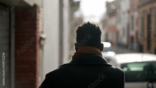 Back of elegant black man walking in city sidewalk during winter season removing scarf