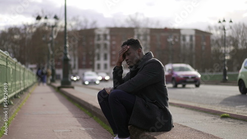 Anxious black man sitting on sidewalk feeling worried