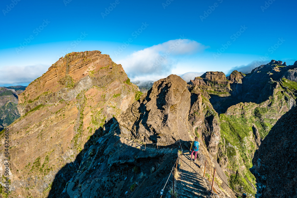 Woman hiking down steep stairs along scenic hike trail to Pico Ruivo in the morning. Pico do Arieiro, Madeira Island, Portugal, Europe. Woman hiking down steep stairs along scenic hike trail to Pico Ruivo in the morning. Pico do Arieiro, Madeira Island, Portugal, Europe.