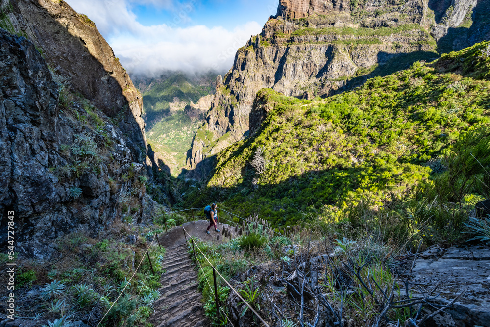 Fototapeta premium Woman with backpack hiking down stairs along scenic hike trail to Pico Ruivo in the morning. Pico do Arieiro, Madeira Island, Portugal, Europe.