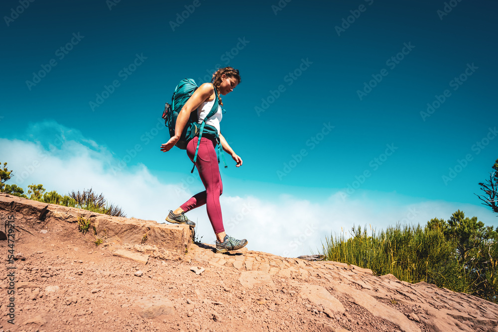 Hiker with backpack walking down a step along the hiking trail on Pico Ruivo. Verade do Pico Ruivo, Madeira Island, Portugal, Europe.