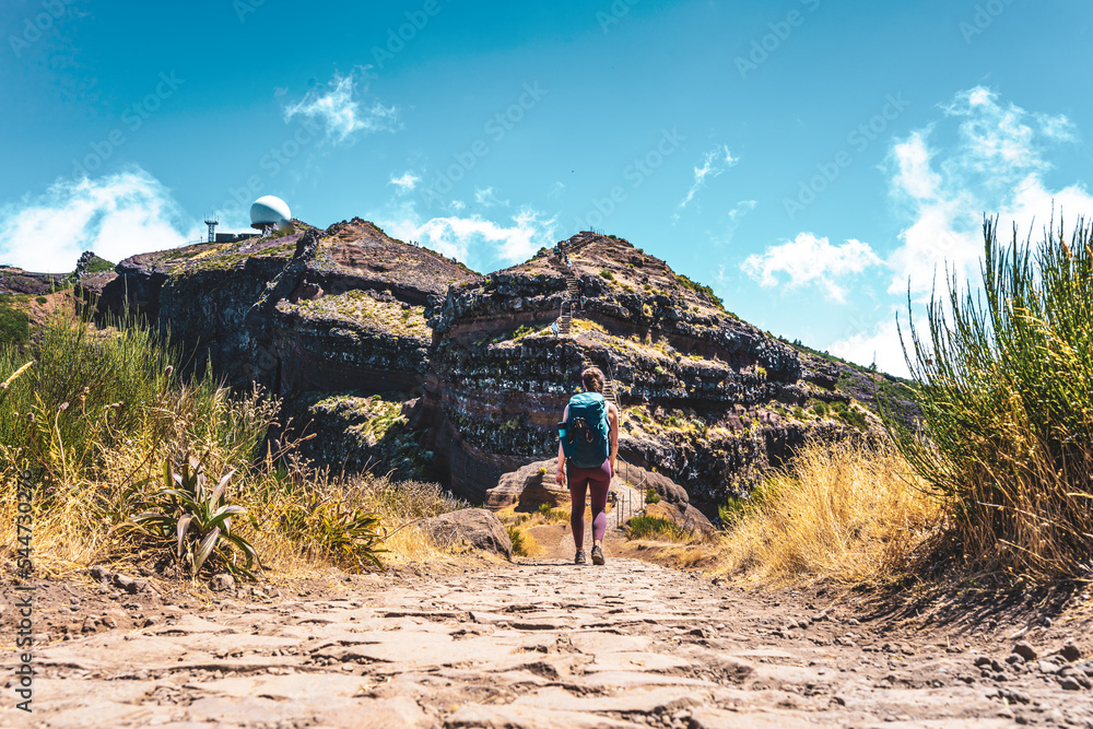 Naklejka premium Sportive woman with backpack walking along scenic hike trail to Pico do Ariero in the afternoon. Verade do Pico Ruivo, Madeira Island, Portugal, Europe.