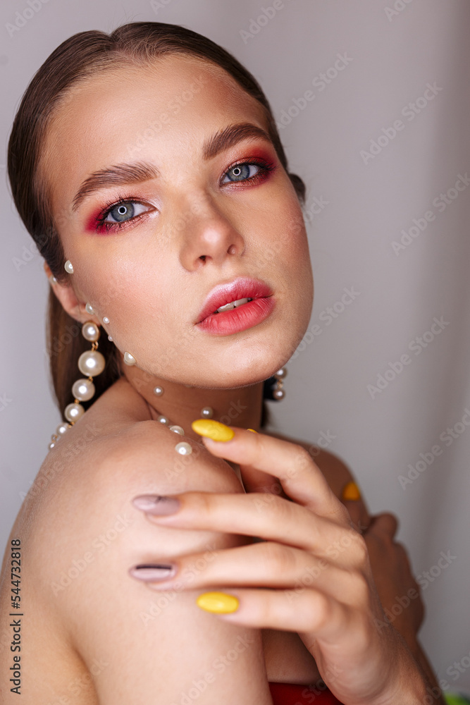 Side view portrait of beautiful woman with makeup and in pearl earrings touching shoulder and looking at camera in studio on white background 