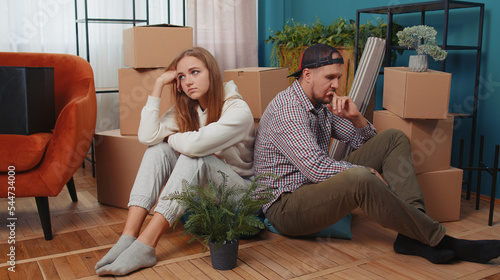 Sad tired married couple man woman leave house sit on floor near cardboard boxes with belongings stuff. Long relocation, bankruptcy, bank debt, eviction, division of property, divorce, hard moving day