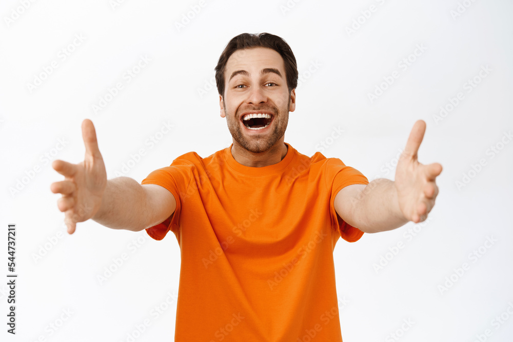 Enthusiastic young man inviting you to hug, extending hands, reaching to you and smiling, cuddling, standing over white background Enthusiastic young man inviting you to hug, extending hands, reaching to you and smiling, cuddling, standing over white background
