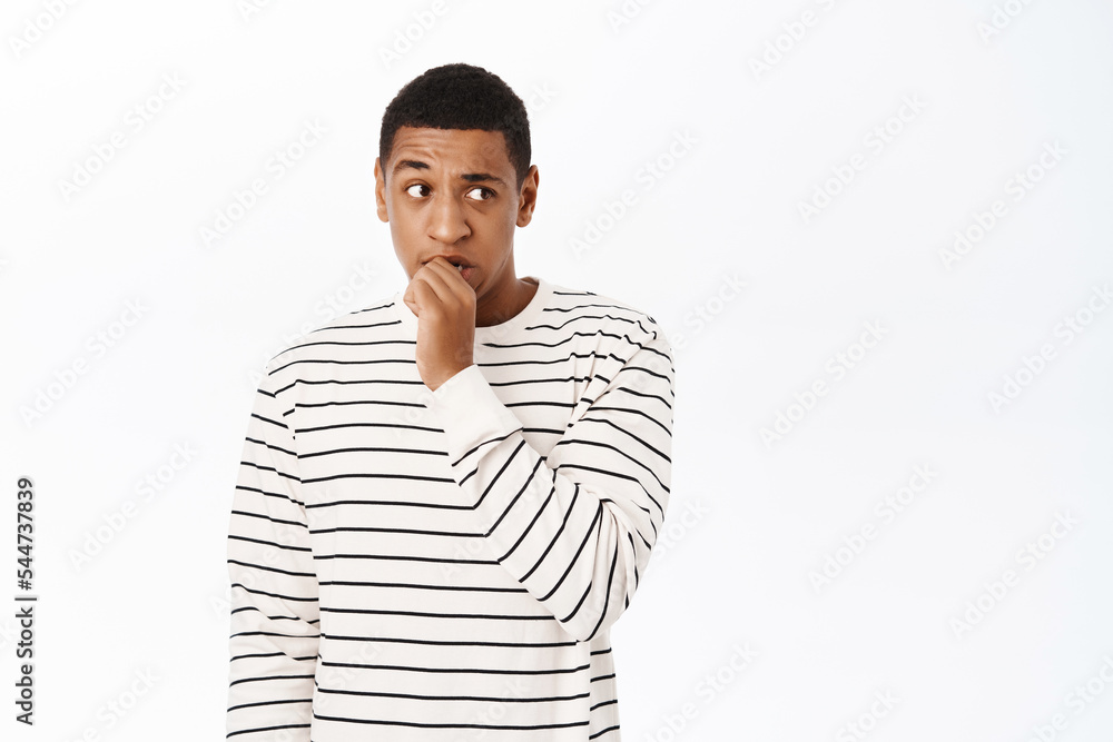 Anxious middle aged african american man, biting fingers, looking scared or nervous, standing over white background Anxious middle aged african american man, biting fingers, looking scared or nervous, standing over white background