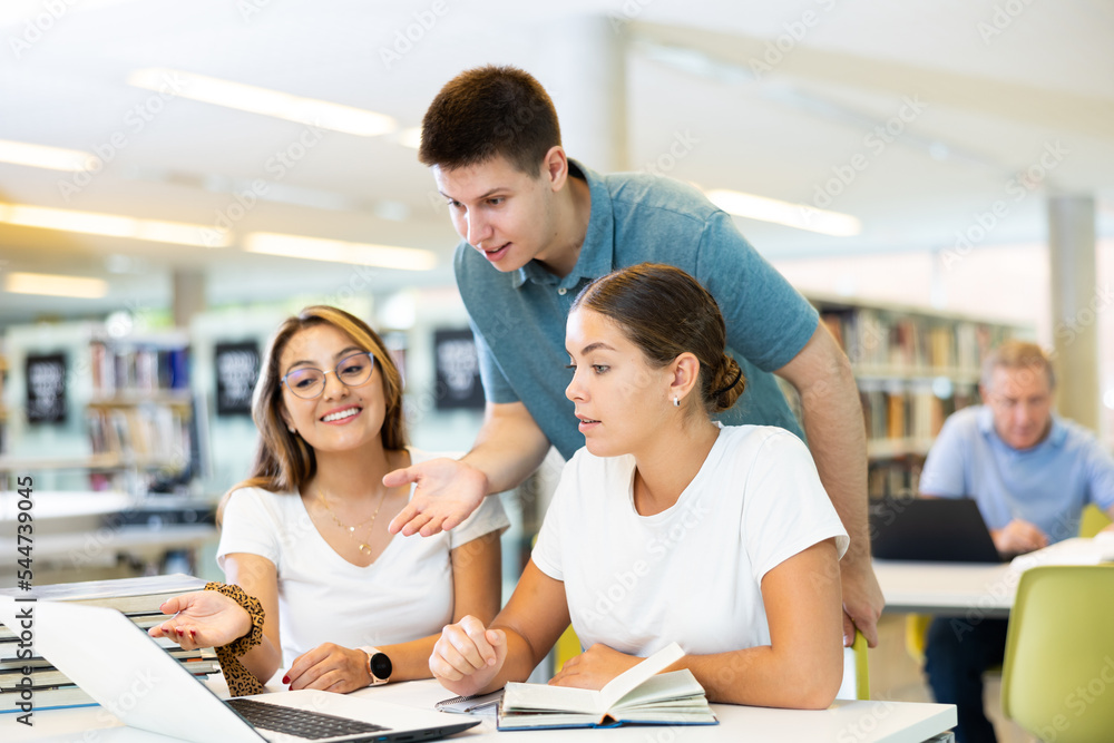 Obraz premium Young man explaining info to young women poiting on the screen of computer in the library