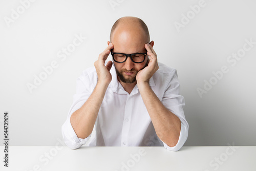 Young man with closed eyes holding on to the weights while sitting at the table on a white background