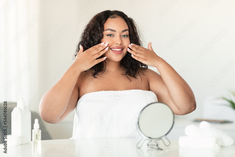 Young african american plus size lady touching her face while making facial treatments in bedroom, copy space Young african american plus size lady touching her face while making facial treatments in bedroom, copy space