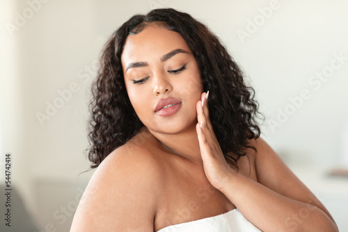 Attractive african american plus size woman touching her face and enjoying silky touch after using new nourishing cream