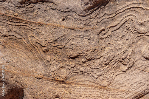 Stone wall with wavy patterns and various bright and dark spots. Textured stone background of sand color with wavy patterns.