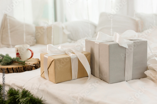 Christmas gifts on the bed on a white sheet. Spruce branch. Cozy morning.