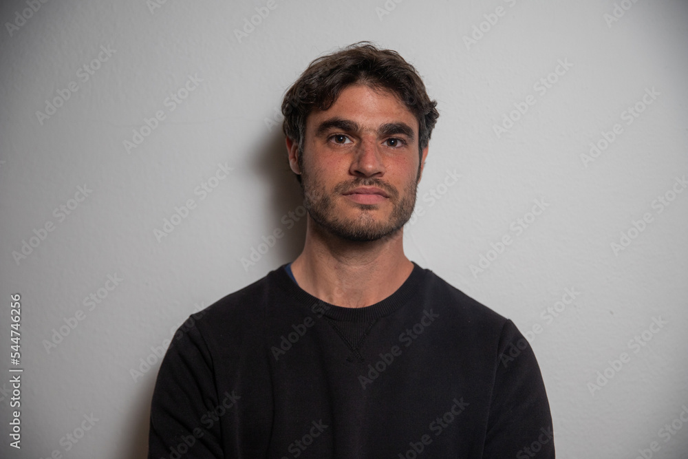 Portrait of a dark-haired and bearded young man resting on the wall at the studio