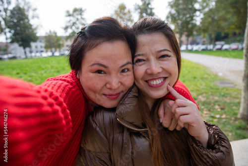 Two gorgeous smiling chinese female friends take a selfie at a public park