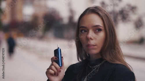 Slow motiion shot of Young woman smoke electronic cigarette outdoors. Female inhales vapor of electronic cigarette and cough. photo