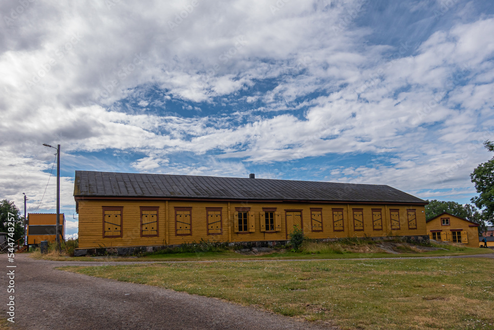 Helsinki, Finland - July 19, 2022: Suomenlinna Fortress. Long yellow building with most windows shuttered under blue cloudscape. Green lawn and gravel path up front