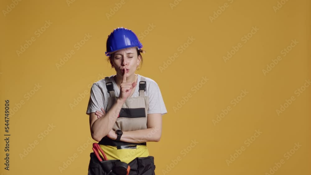 Portrait of construction worker doing hush mute sign, advertising silence and privacy gesture. Female constructor keeping secret and showing confidential symbol over studio background. Portrait of construction worker doing hush mute sign, advertising silence and privacy gesture. Female constructor keeping secret and showing confidential symbol over studio background.