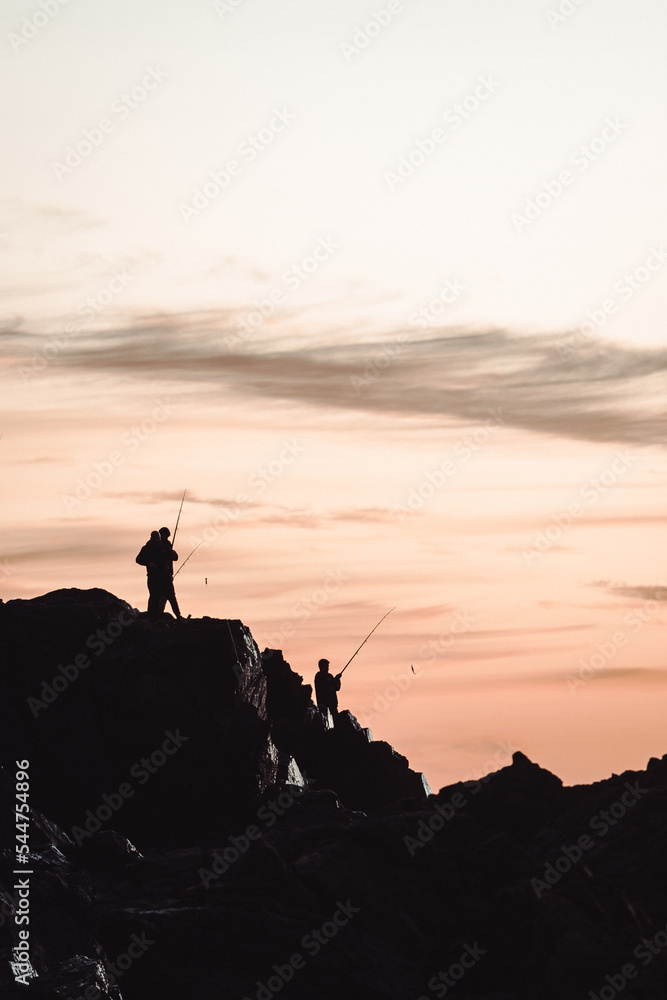 silhouette of a person on a rock fishing