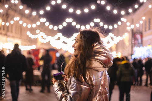 Happy young woman standing in city street during Christmas holidays at night