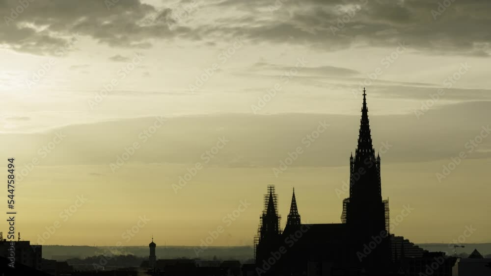 Time lapse shot with the silhouette of the Ulm minster in front of a yellow sky at morning with some clouds Time lapse shot with the silhouette of the Ulm minster in front of a yellow sky at morning with some clouds