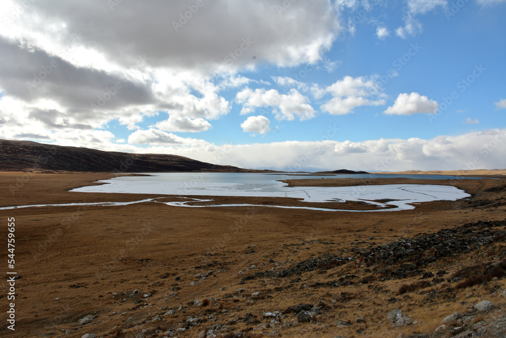 A lake bound by the first ice, surrounded by mountain ranges in the autumn steppe under a cloudy sky.