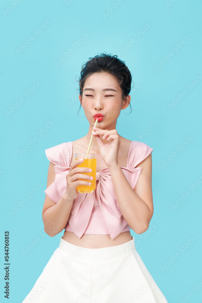 Portrait of a cute casual girl drinking orange juice from a glass over blue background Portrait of a cute casual girl drinking orange juice from a glass over blue background