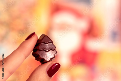 Advent chocolate Christmas tree, girl holding a festive praline, yellow bokeh bg